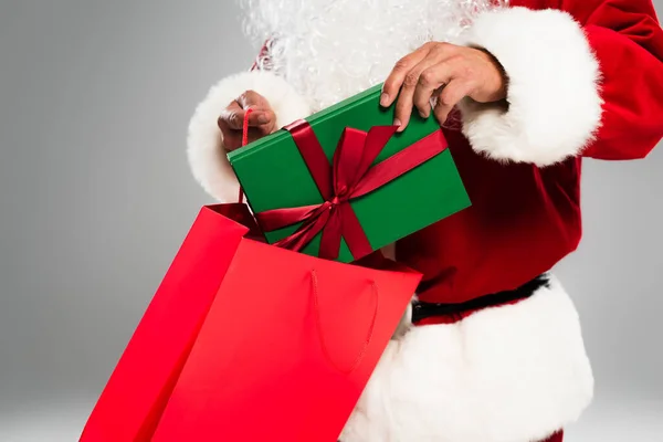 Vista cortada de Papai Noel barbudo colocando presente em saco de compras isolado em cinza — Fotografia de Stock
