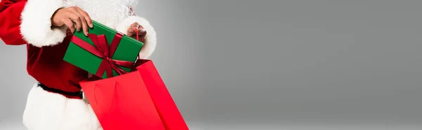 Cropped view of father christmas putting gift in shopping bag isolated on grey, banner — Stock Photo