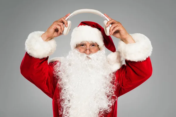 Father christmas in costume holding wireless headphones isolated on grey — Stock Photo