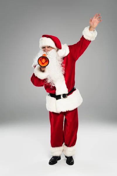 Full length of santa claus in red costume holding loudspeaker on grey background — Stock Photo