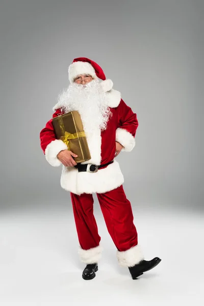 Piena lunghezza di Babbo Natale con presente in piedi su sfondo grigio — Foto stock