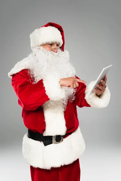 Santa claus in eyeglasses pointing at digital tablet isolated on grey — Stock Photo