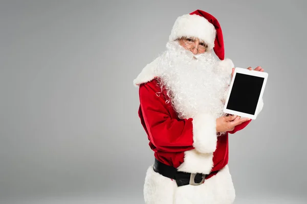 Санта-Клаус в костюмі тримає цифровий планшет з порожнім екраном ізольовано на сірому — стокове фото