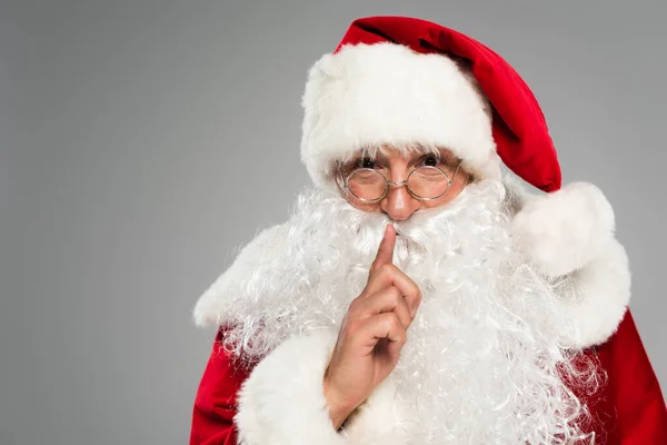 Retrato de Papá Noel mostrando gesto secreto a cámara aislada en gris - foto de stock