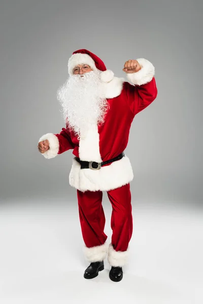 Toute la longueur de barded santa claus danser et regarder la caméra sur fond gris — Photo de stock