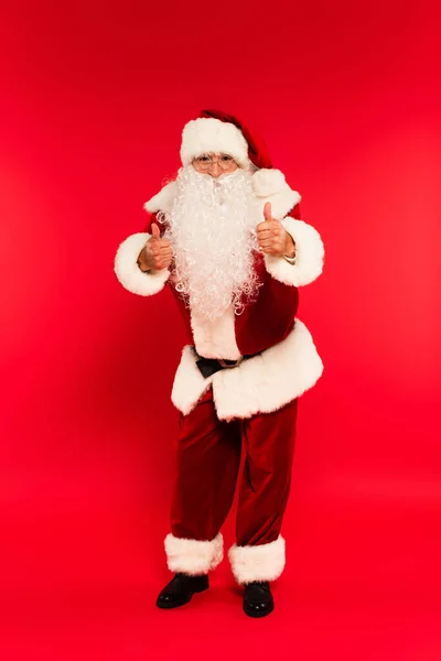 Santa Claus en anteojos mostrando como gesto a cámara sobre fondo rojo - foto de stock