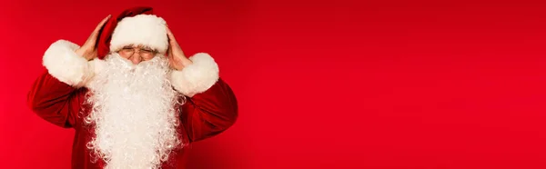 Bearded santa claus in eyeglasses touching head on red background with copy space, banner — Stock Photo