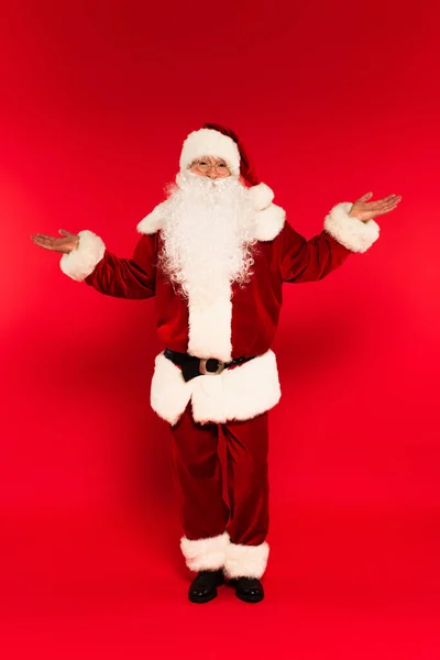 Père Noël en costume pointant avec les mains sur fond rouge — Photo de stock