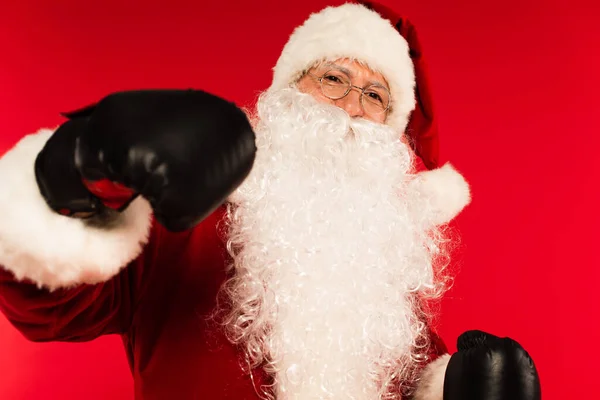 Babbo Natale in occhiali e guanti da boxe guardando la fotocamera isolata sul rosso — Foto stock