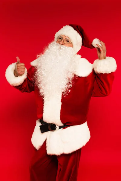 Санта Клаус трогает шляпу и показывает, как жест на красном фоне — стоковое фото