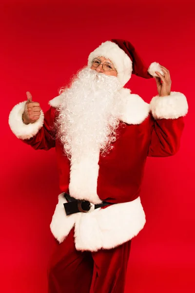 Santa claus tocando sombrero y mostrando como gesto sobre fondo rojo - foto de stock