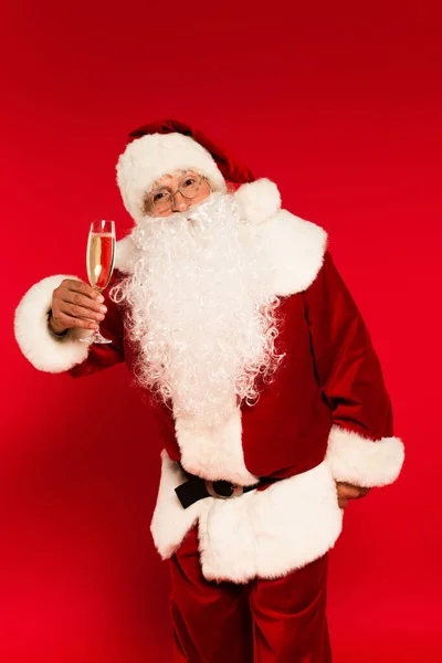 Santa Claude en lunettes et costume tenant verre de champagne sur fond rouge — Photo de stock