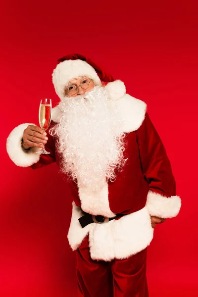 Santa claus in eyeglasses and costume holding champagne glass on red background — Stock Photo