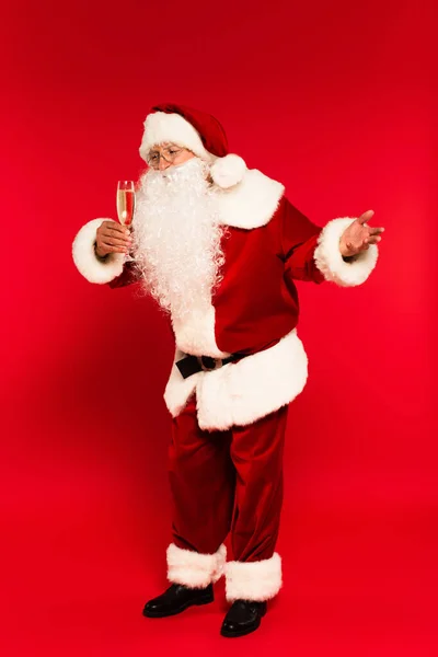 Pleine longueur de Santa Claus regardant une coupe de champagne sur fond rouge — Photo de stock