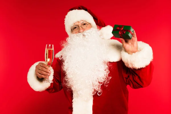 Father christmas holding champagne glass and present on red background — Stock Photo