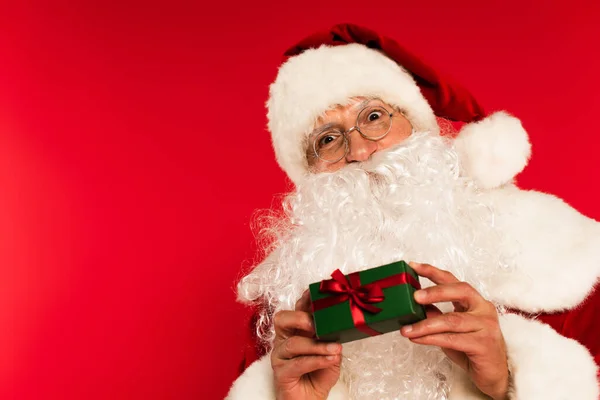 Barbudo padre navidad celebración pequeña caja de regalo aislado en rojo - foto de stock