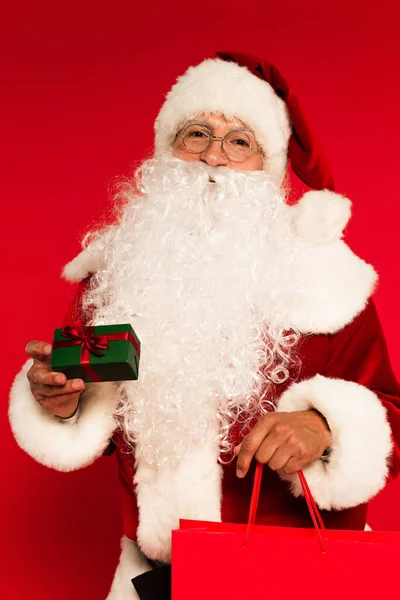 Weihnachtsmann mit Einkaufstasche und kleinem Geschenk auf rotem Hintergrund — Stockfoto