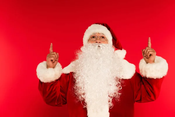 Santa claus in eyeglasses pointing with fingers on red background — Stock Photo