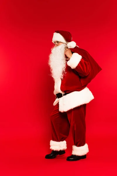 Full length of father chistmas holding sack on red background — Stock Photo