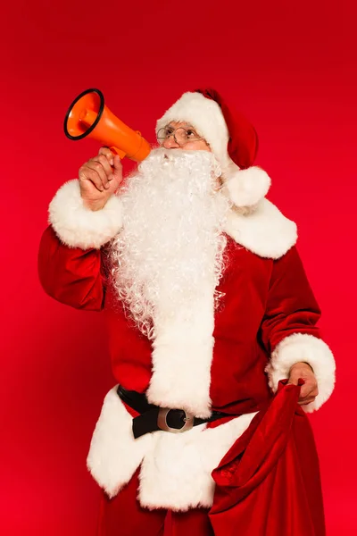 Père Noël tenant haut-parleur et sac sur fond rouge — Photo de stock
