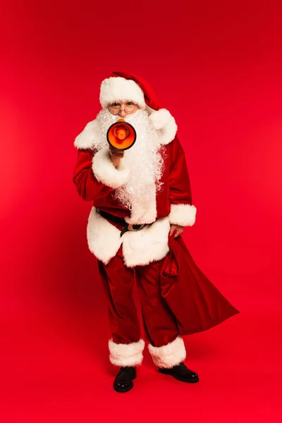 Father christmas in costume holding sack and loudspeaker on red background — Stock Photo