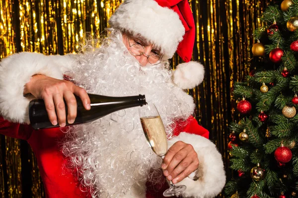 Barbu santa claus verser du champagne près de sapin et tinelle floue — Photo de stock