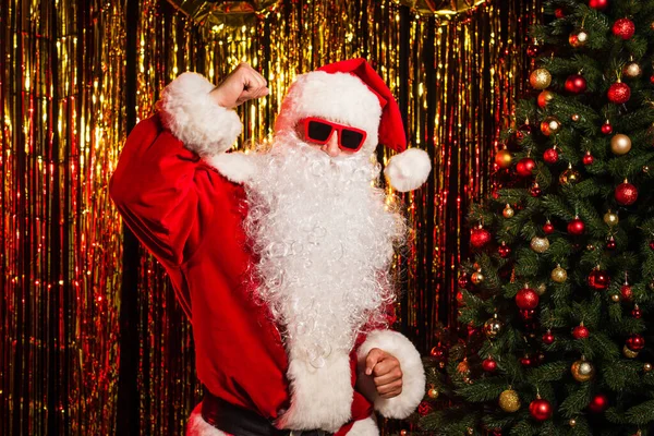 Père Noël en lunettes de soleil et costume dansant près de l'arbre de Noël et tinsel — Photo de stock