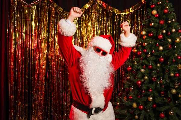 Батько Різдво в сонцезахисних окулярах танцює під час вечірки біля сосни і мішури — стокове фото