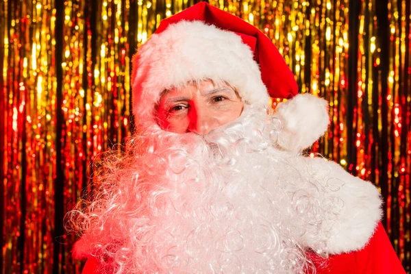 Portrait of bearded santa claus in hat looking at camera near blurred tinsel — Stock Photo
