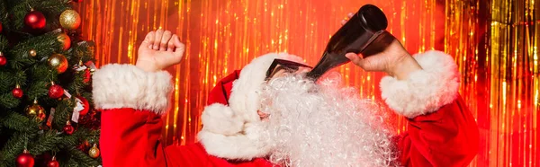 Padre Navidad en gafas de sol beber champán de botella cerca de oropel, pancarta - foto de stock