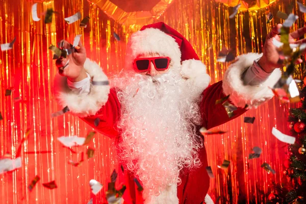 Babbo Natale in occhiali da sole lanciare coriandoli durante la festa vicino orpelli — Foto stock