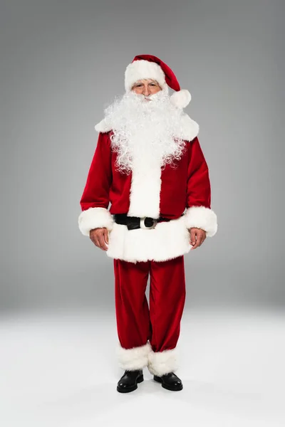 Full length of bearded father christmas looking at camera while standing on grey — Stock Photo