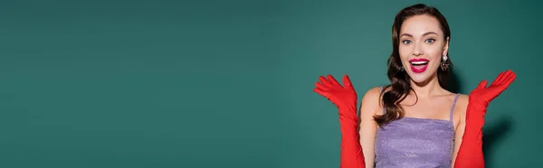 Erstaunte junge Frau mit roten Lippen und Handschuhen gestikulierend auf grünem Hintergrund, Banner — Stockfoto