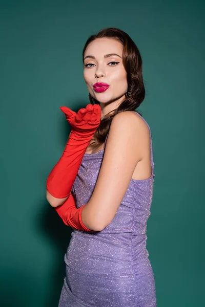 Красива молода жінка в червоних рукавичках і фіолетовій сукні, що посилає повітряний поцілунок на зеленому — стокове фото