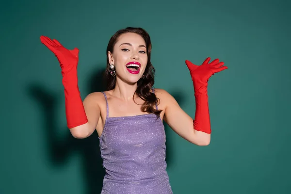 Excited young woman in bright gloves and purple dress gesturing while looking at camera on green — Stock Photo