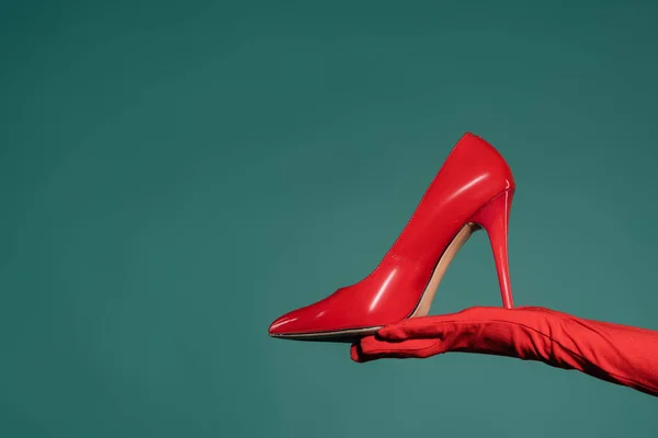 Cropped view of woman in red glove holding high heeled shoe on green background — Stock Photo