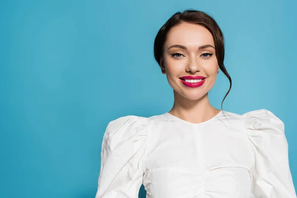 Charmante junge Frau in weißer Bluse lächelt, während sie vereinzelt in die Kamera auf blau blickt — Stockfoto