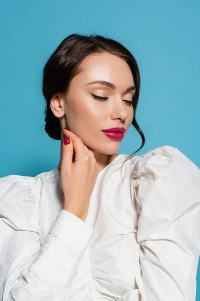 Sensuelle et jeune femme avec maquillage touchant visage isolé sur bleu — Photo de stock