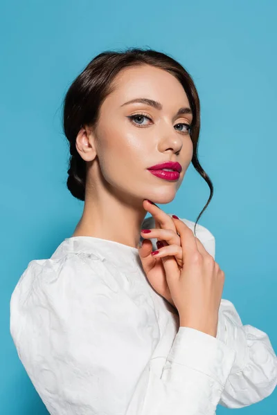 Portrait of brunette young woman in white blouse looking at camera isolated on blue — Stock Photo