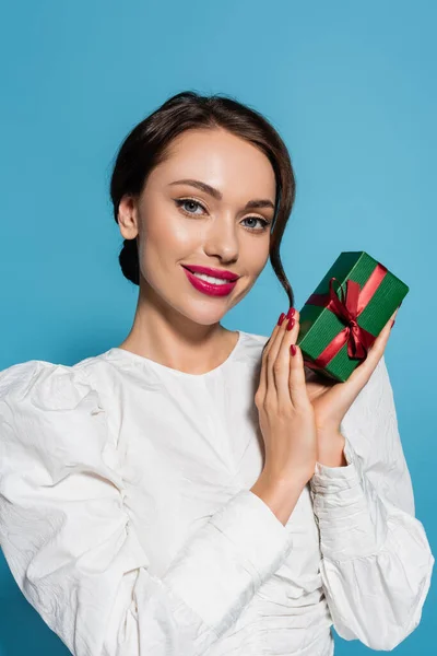 Cheerful young woman in white blouse holding wrapped present on blue — Stock Photo