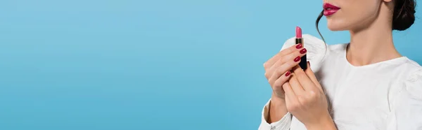 Cropped view of young woman in white blouse holding pink color lipstick isolated on blue, banner — Stock Photo