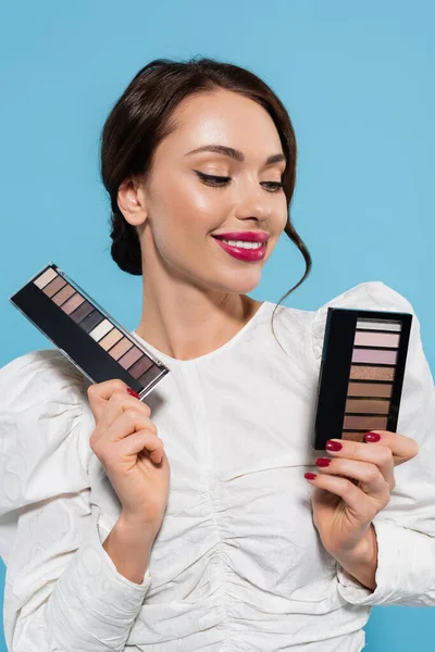Cheerful young woman holding eye shadow palettes isolated on blue — Stock Photo