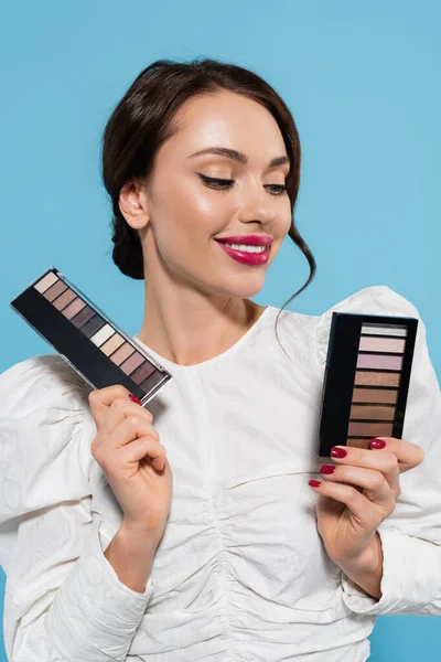 Alegre joven mujer sosteniendo ojos sombra paletas aislado en azul - foto de stock