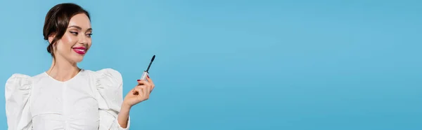 Cheerful young woman in white blouse holding mascara brush isolated on blue, banner — Stock Photo