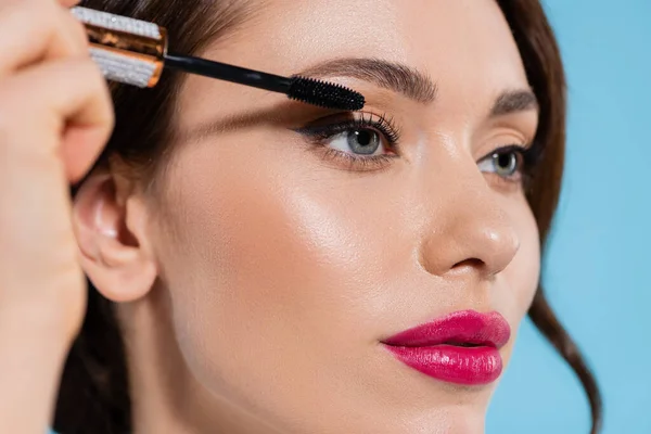 Close up of young woman applying mascara on eyelash isolated on blue — Stock Photo