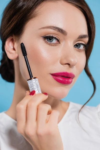 Close up of pretty young woman holding mascara and looking at camera isolated on blue — Stock Photo