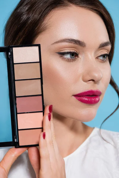 Portrait de jolie jeune femme en chemisier blanc tenant la palette de blush isolé sur bleu — Photo de stock