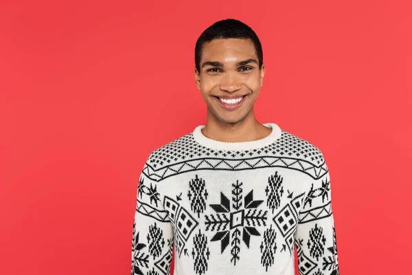 Front view of happy african american man in knitted sweater with winter ornament isolated on red — Stock Photo