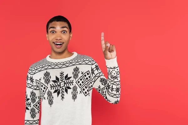 Cheerful african american man in white sweater with winter pattern showing idea sign isolated on red — Stock Photo