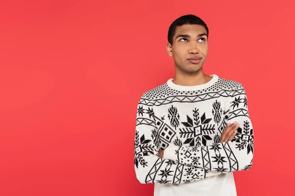 Riflessivo uomo afroamericano in caldo maglione in piedi con le braccia incrociate e distogliendo lo sguardo isolato sul rosso — Foto stock